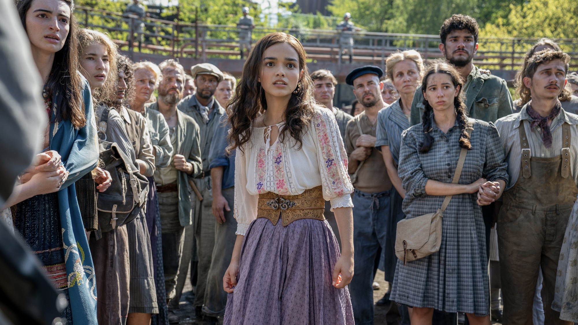 A young woman in a colorful dress looks terrified while surrounded by a crowd.