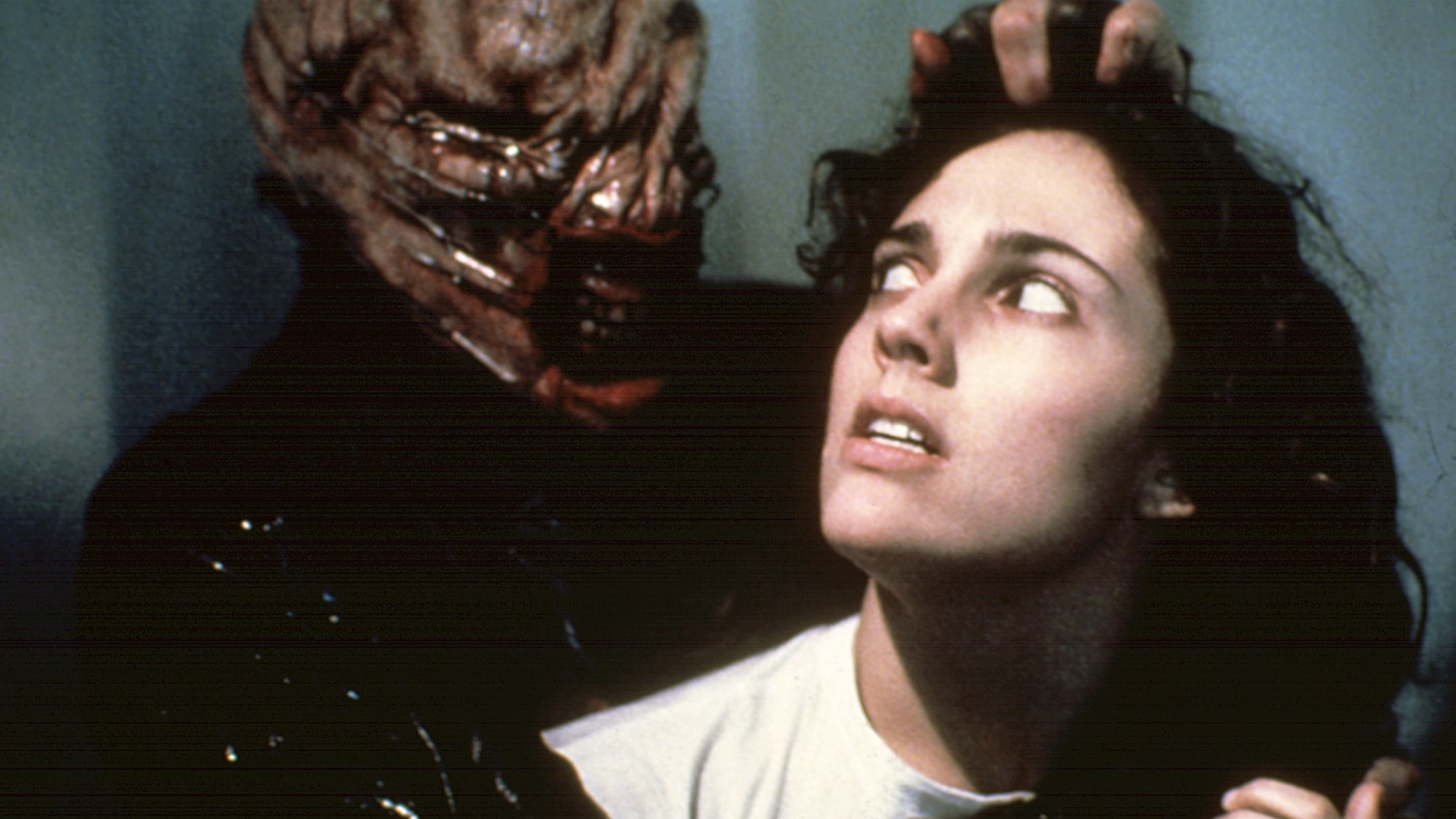 A scene from Hellraiser, where a scared young white woman is being tortured by a moist-looking skinless monster.