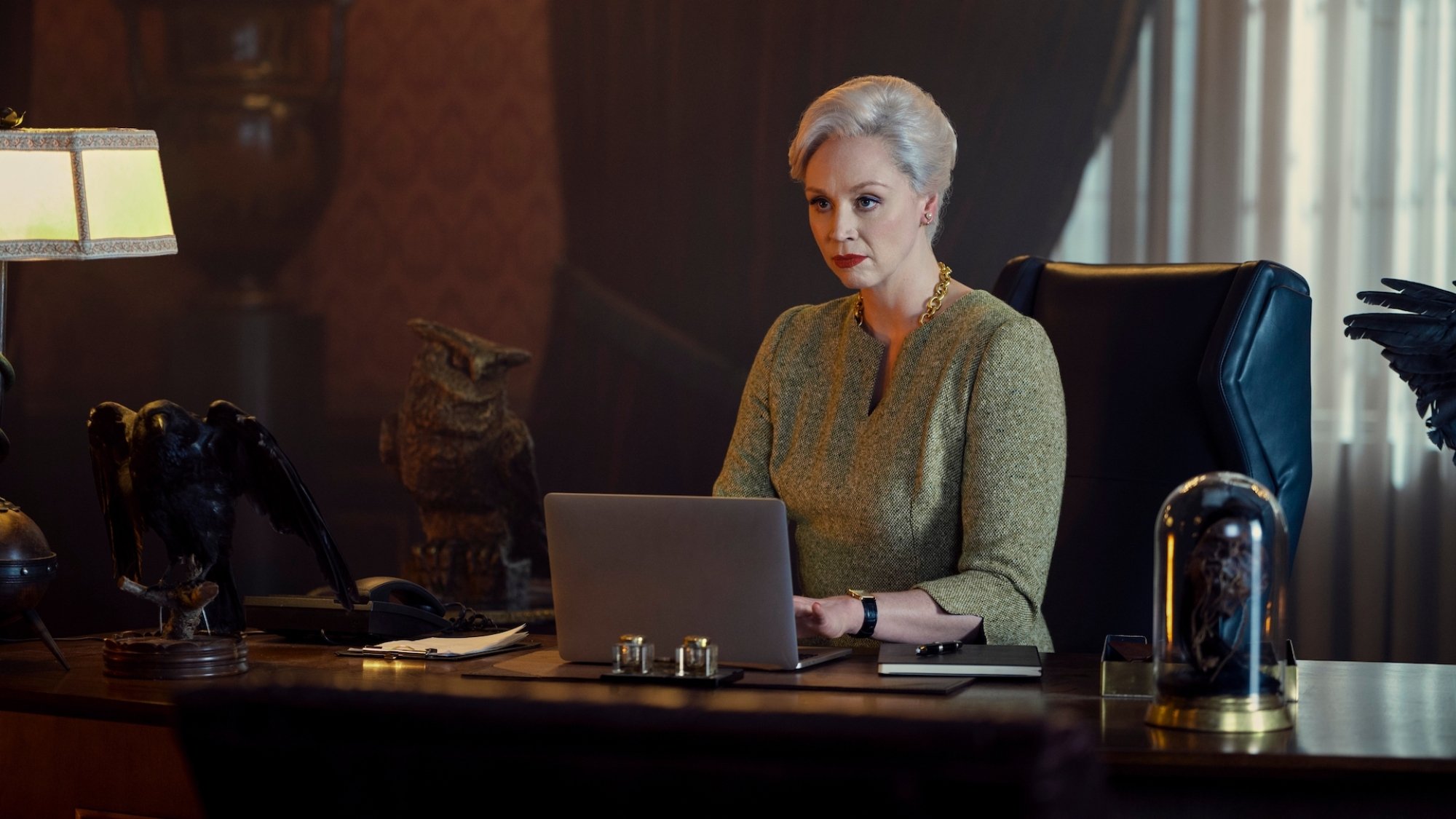 A woman dressed elegantly sits behind a laptop at her impressive principal desk.