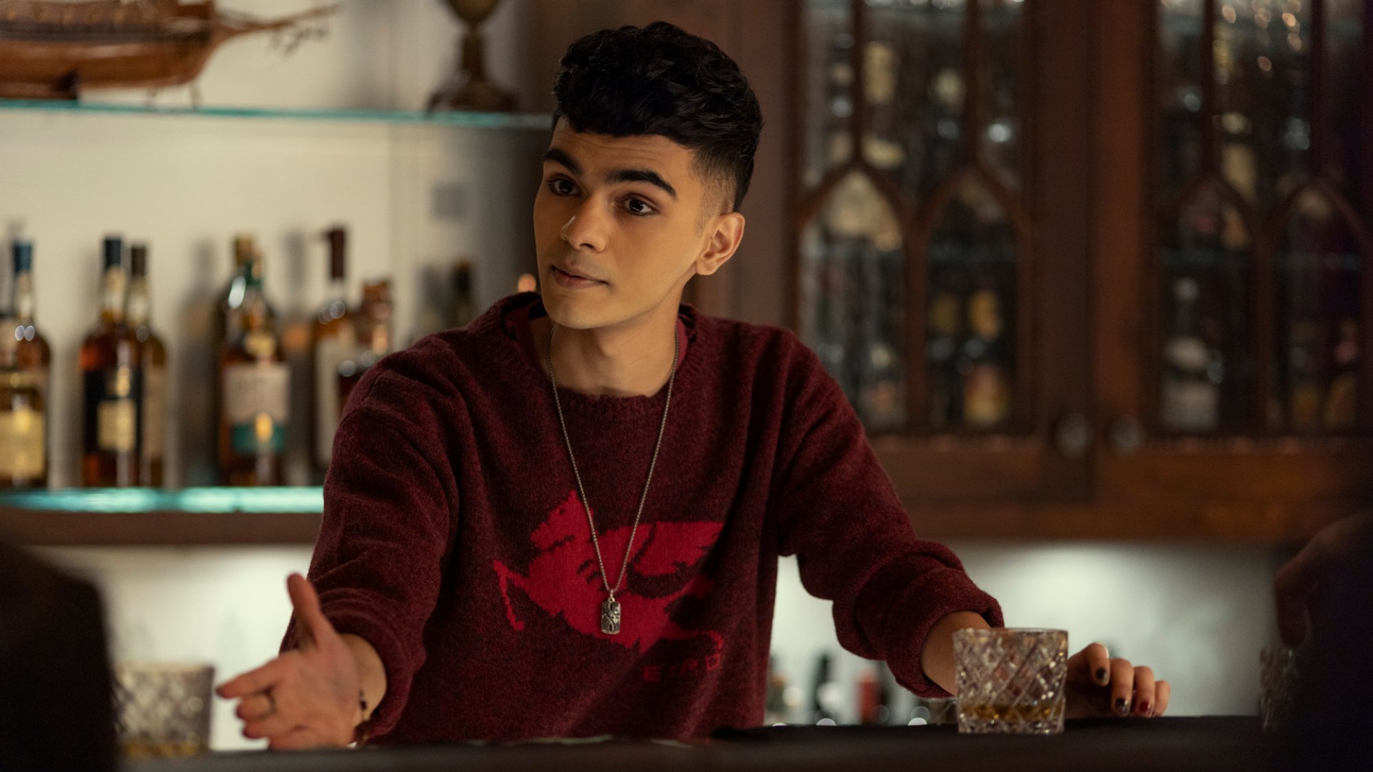 A young man in a red t-shirt stands behind a bar.