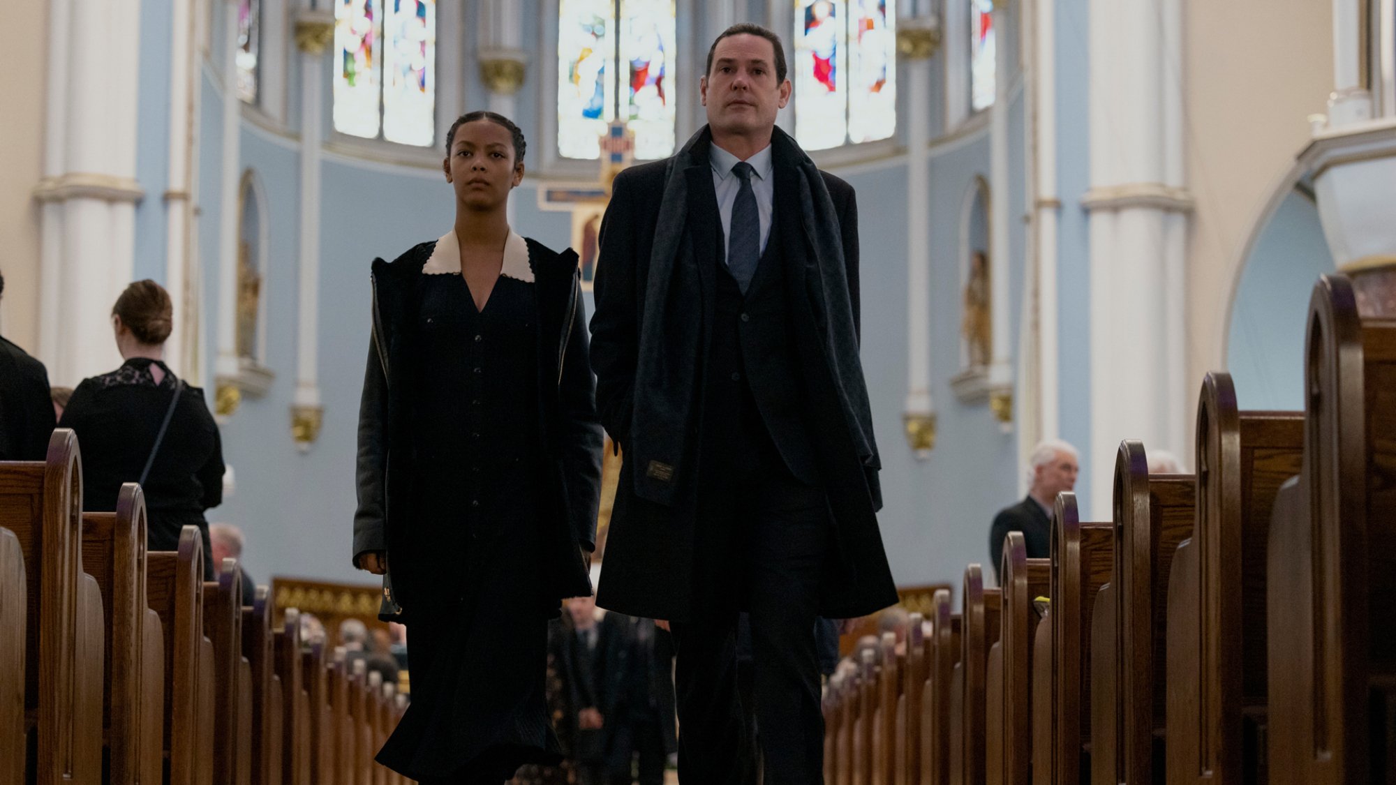 A man and a young girl walk down a church aisle at a funeral.