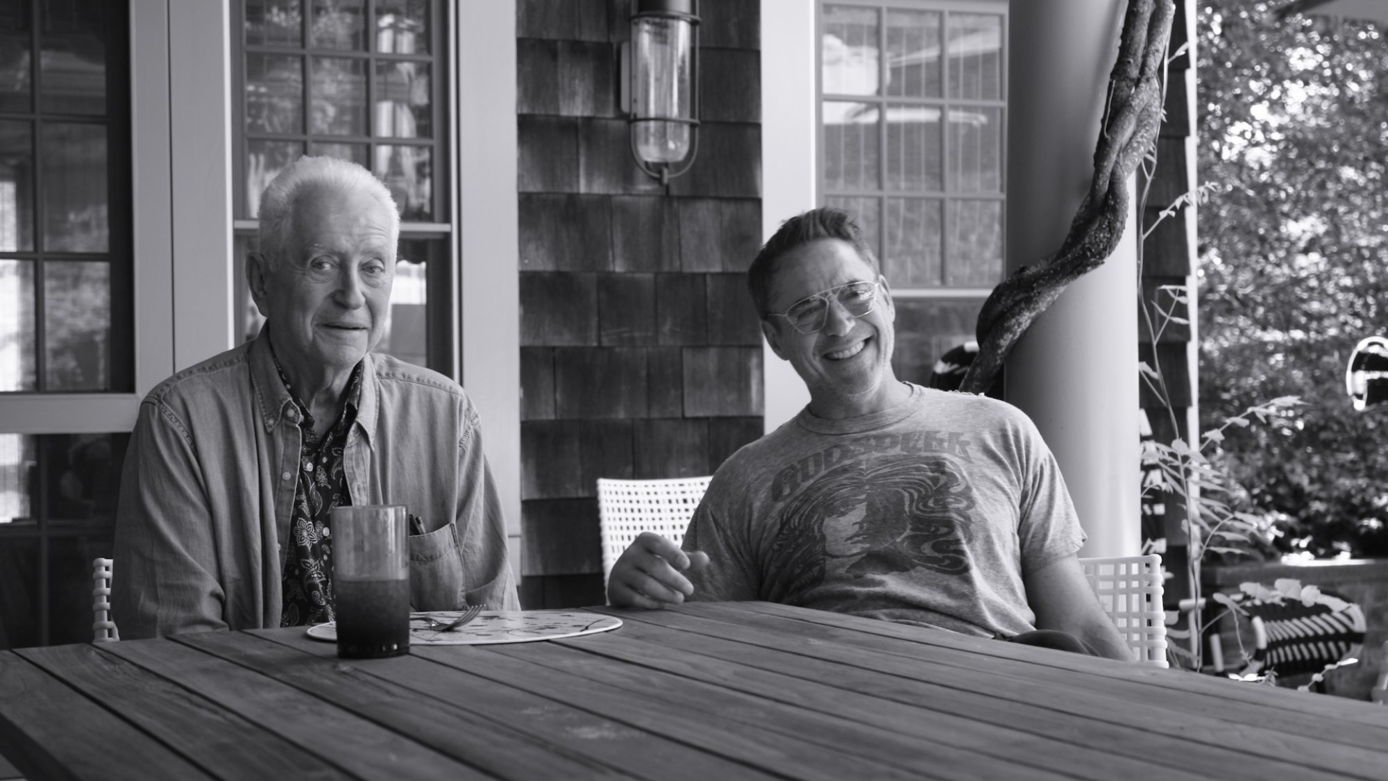 Robert Downey Sr. and Robert Downey Jr. sit together at a table on a porch.