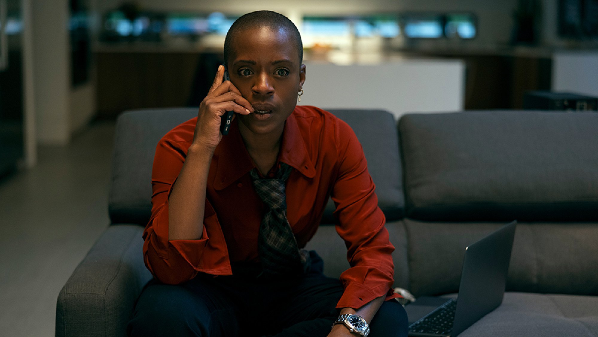 A woman sits on a sofa holding a phone to her ear.
