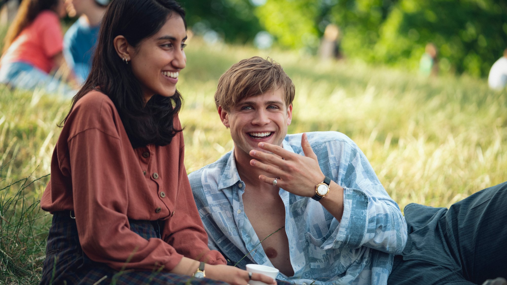 A young man and woman sit giggling in the park.