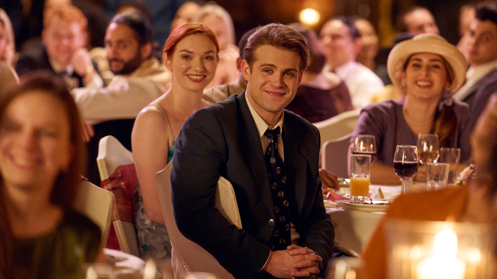A young man sits in a wedding crowd during a speech.