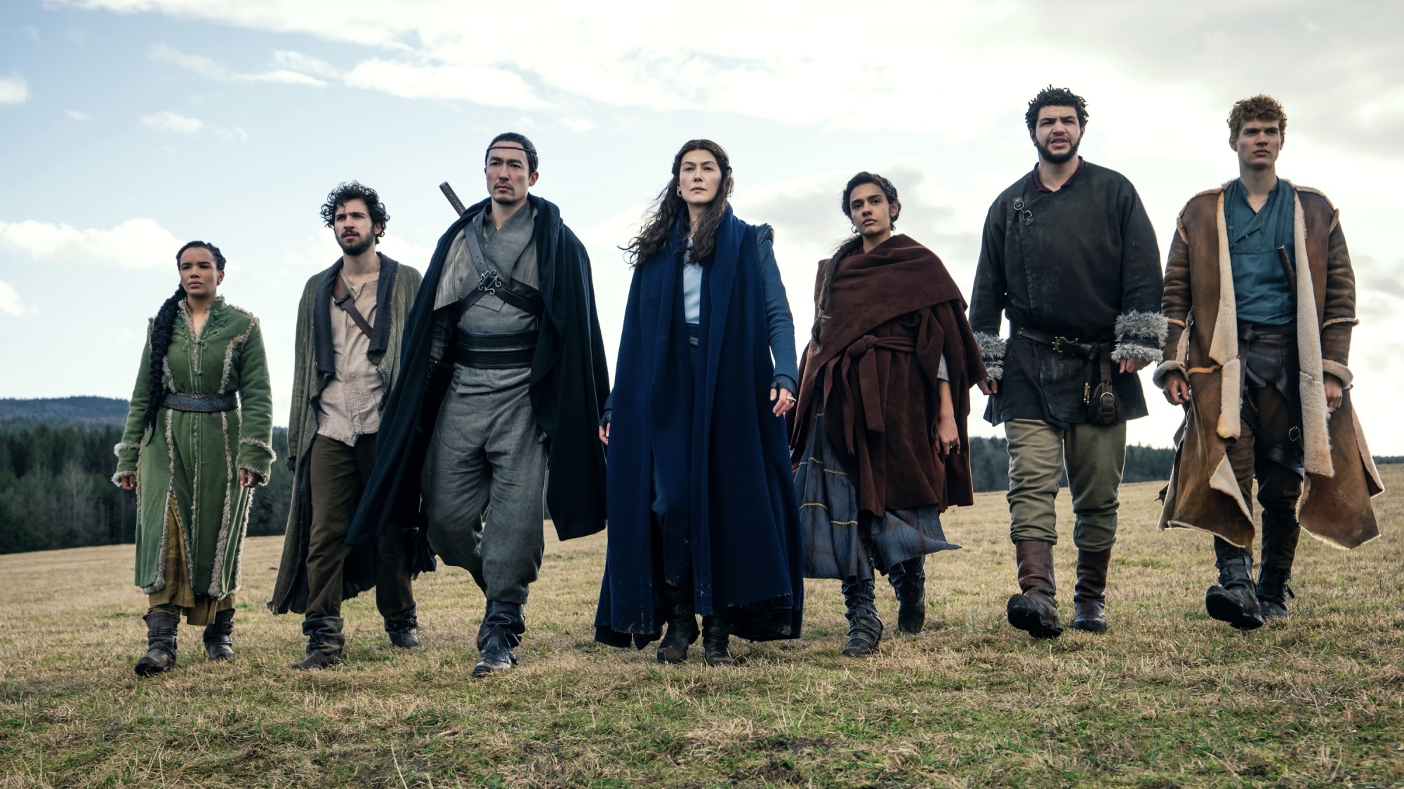 A group of four men and three women walk across a green grass field.