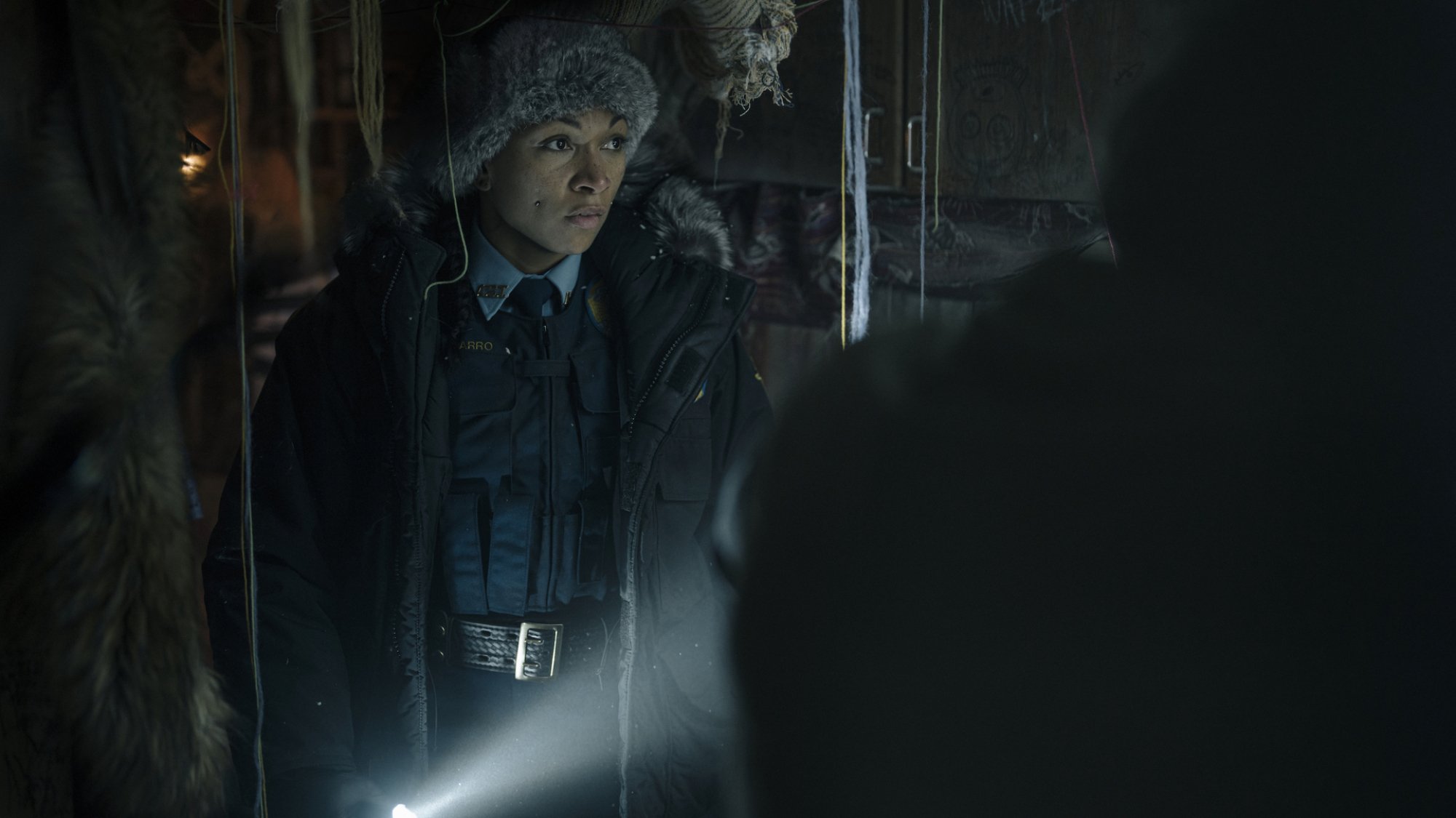 A state trooper walks through a dark space with a flashlight.